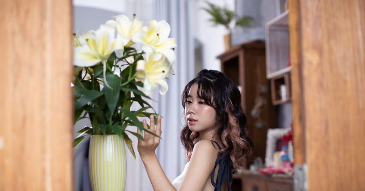 A serene indoor portrait of a woman seated beside a vase of white lilies, evoking elegance and tranquility.